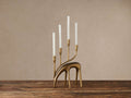 Antiqued brass Grazing Deer Taper Holder with four white taper candles on a rustic wooden table.
