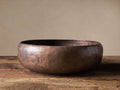 Hand Hammered Copper Bowl, round and shallow, with a textured, mottled reddish-brown finish, resting on rustic wood.