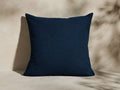 Harborside Outdoor Pillow. Textured navy blue bouclv© square pillow, upright, on a light surface with plant shadows.