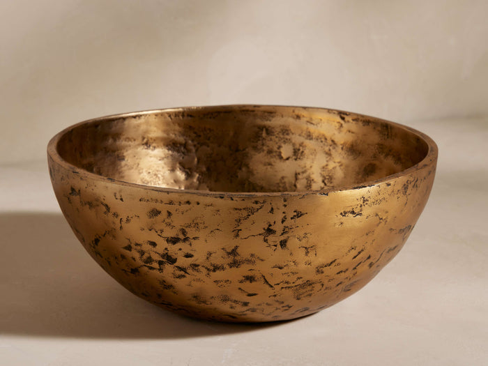 Harper Bowl: A decorative, round, brass-finished aluminum bowl with a distressed, hammered texture, shown slightly from above.