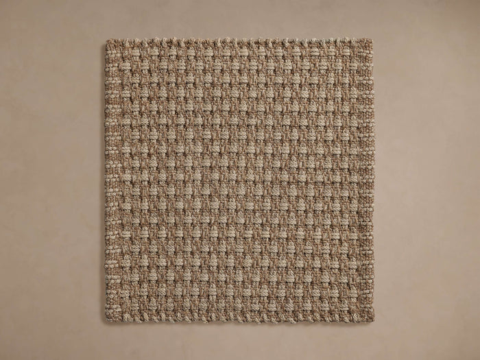 Hatcher Outdoor Rug Swatch. Rectangular, woven swatch in two-tone beige and light brown, laid flat on a light brown surface.