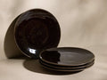Front view of dark chocolate Hearthline Dinner Plates, one upright, three stacked, with reactive glaze finish.