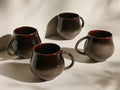 Four Heartline Mugs in dark brown to speckled tan gradient, with rounded bodies and handles, arranged on a light surface.