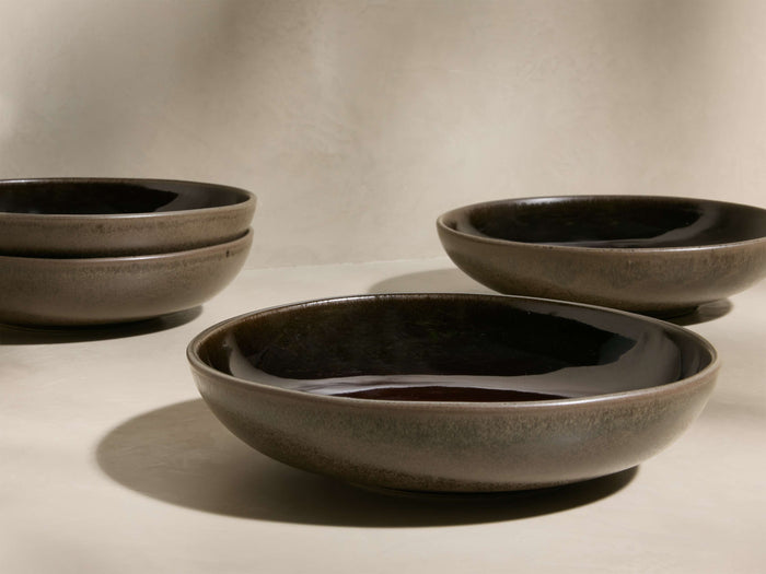 Four dark gray Hearthline Pasta Plates: two stacked on the left, and two individually placed on the right.