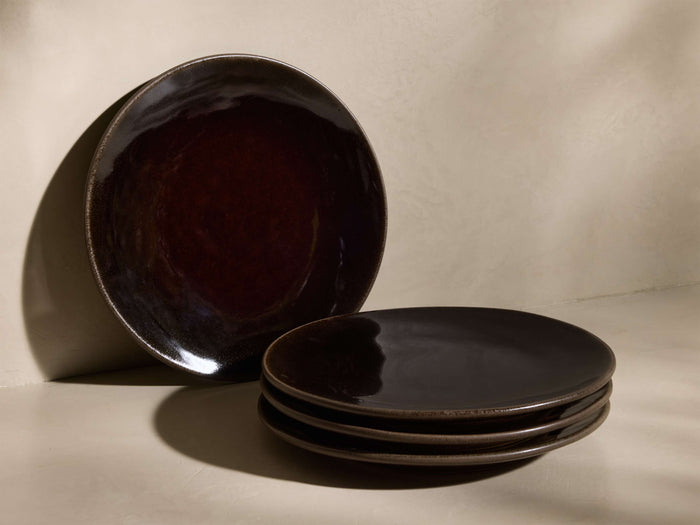 One mocha brown Hearthline Salad Plate (Set of 4) with glossy reactive glaze stands upright, three are stacked flat.