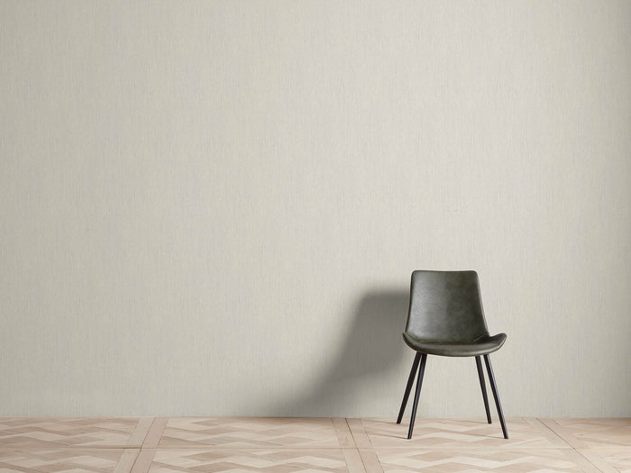 Heath Faux Grasscloth Wallpaper with subtle woven texture in a neutral tone, covering a wall behind a dark green chair on patterned flooring.