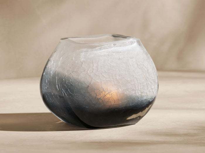 Indigo Tealight Holder. Round, crackled glass with frosted white fading to deep indigo. Warm glow inside on a light surface.