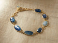 Indira Kyanite Bracelet with blue kyanite and aquamarine stones in gold-plated settings on a fabric background.