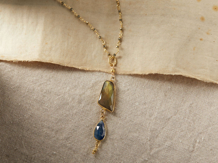 Indira Labradorite Necklace with a gold-vermeil chain featuring labradorite and kyanite stones, accented by pyrite beads, on a fabric background.