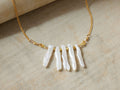 Isar Necklace: Gold chain with five irregular white freshwater pearls and small gold beads, laid flat on a light fabric.