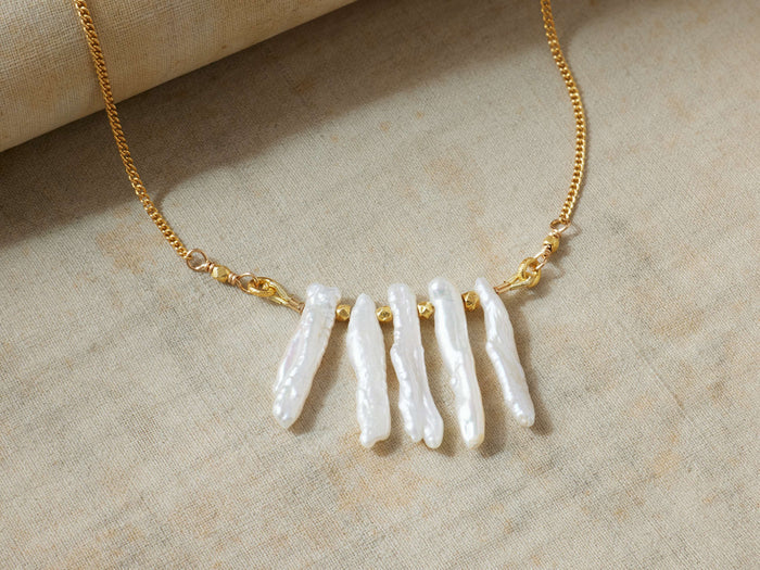 Isar Necklace: Gold chain with five irregular white freshwater pearls and small gold beads, laid flat on a light fabric.