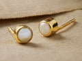 Pair of Isar Stud Earrings. Each features a white freshwater pearl in a textured golden vermeil setting, resting on tan fabric.