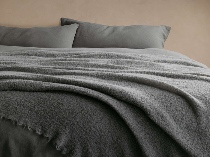 Close-up of the Charcoal Italian Alpaca Boucle Throw draped over a bed, highlighting its soft bouclv© texture.