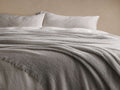 Full view of a light grey Italian Alpaca Boucle Throw, elegantly draped over white bed sheets, showcasing its plush boucle texture.