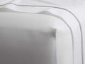 White Italian Percale Fitted Sheet, smooth, with a distinct corner. Fine grey embroidery on an accompanying draped sheet.
