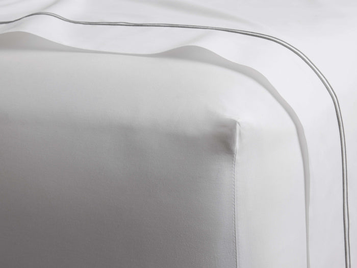 White Italian Percale Fitted Sheet, smooth, with a distinct corner. Fine grey embroidery on an accompanying draped sheet.