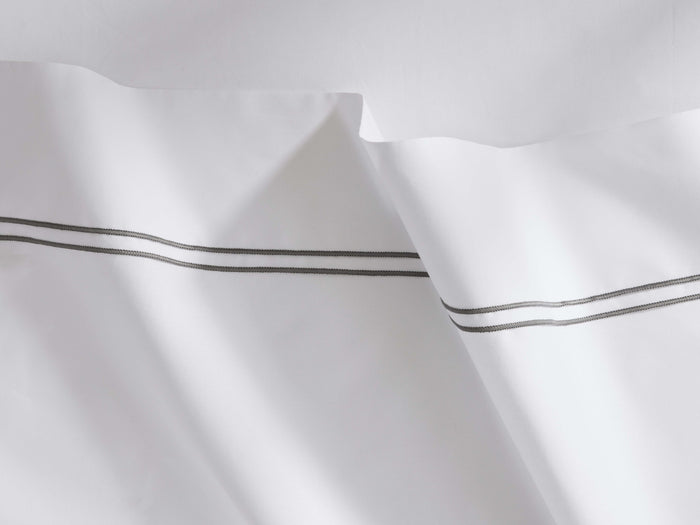 White Italian Embroidered Percale Flat Sheet, draped with two parallel dark grey embroidered lines on the border.