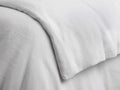 Close-up of a light gray Italian garment-dyed linen duvet, draped with soft folds, highlighting its natural, breathable texture.