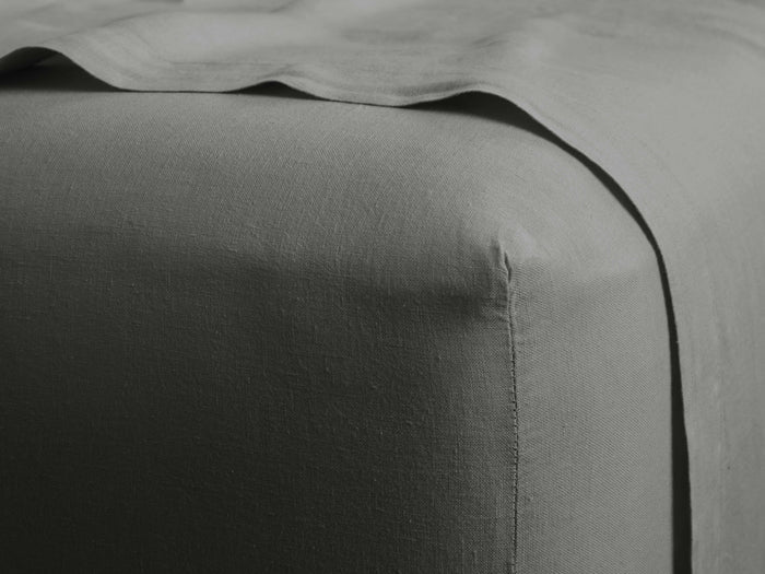 Close-up of a charcoal grey Italian garment-dyed linen fitted sheet on a mattress, highlighting its texture and corner detail.
