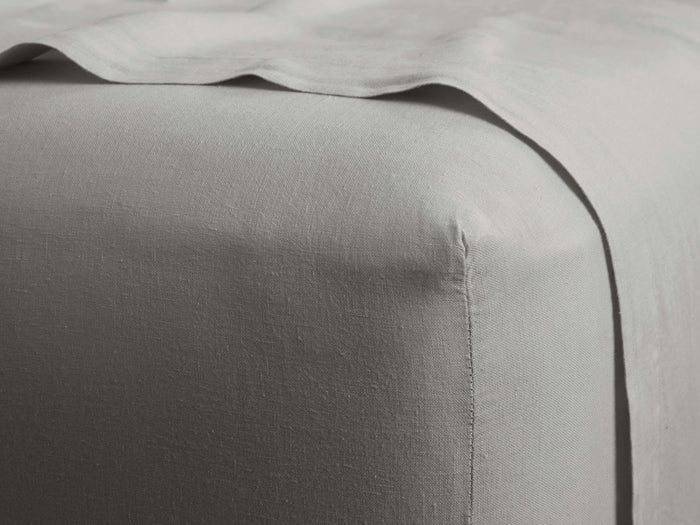 Light grey Garment-Dyed Linen Fitted Sheet on a bed. Visible fabric texture and fitted corner, with a draped sheet above.