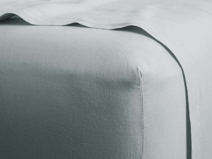 Light blue-grey Italian Garment-Dyed Linen Fitted Sheet on a bed corner with a draped top sheet, highlighting its soft texture.