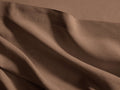 Close-up of a warm brown Italian Garment-Dyed Linen Flat Sheet, draped in soft folds, revealing its natural texture and hem.