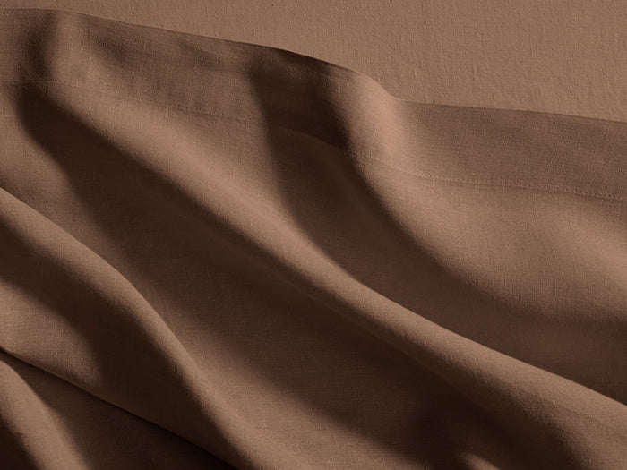 Close-up of a warm brown Italian Garment-Dyed Linen Flat Sheet, draped in soft folds, revealing its natural texture and hem.