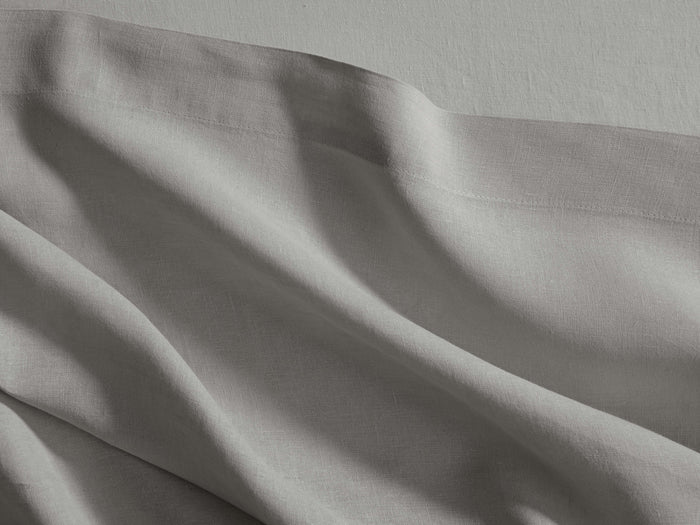 Rumpled light grey Italian Garment-Dyed Linen Flat Sheet, showing soft folds and texture, with a defined hemline.