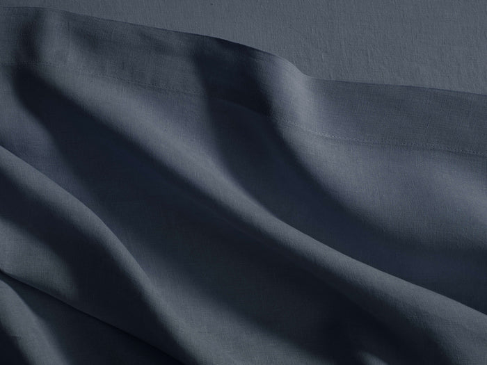 Dark blue Italian garment-dyed linen flat sheet, casually draped with natural folds, showing a subtle hemline stitch.