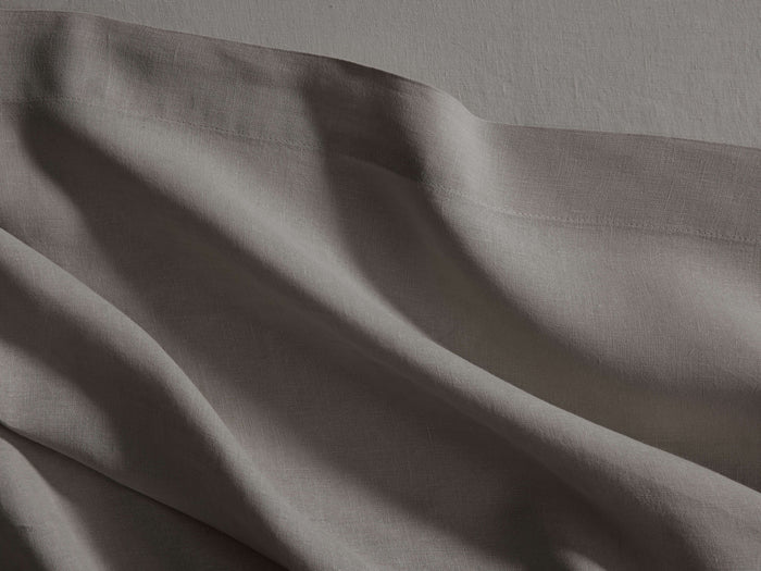 Close-up of a draped Italian Garment-Dyed Linen Flat Sheet in mink, showing soft folds and textured fabric with a hem.