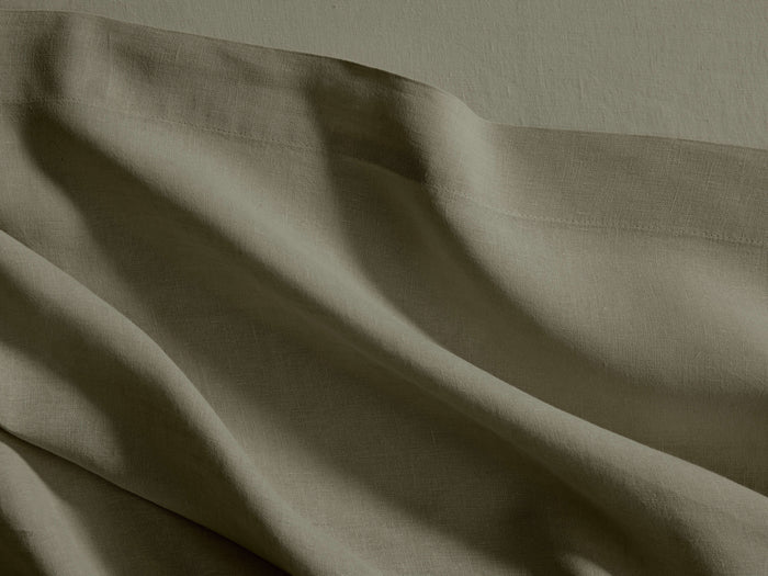 Close-up of olive green Italian Garment-Dyed Linen Flat Sheet, showing its textured fabric, soft folds, and a prominent hem.