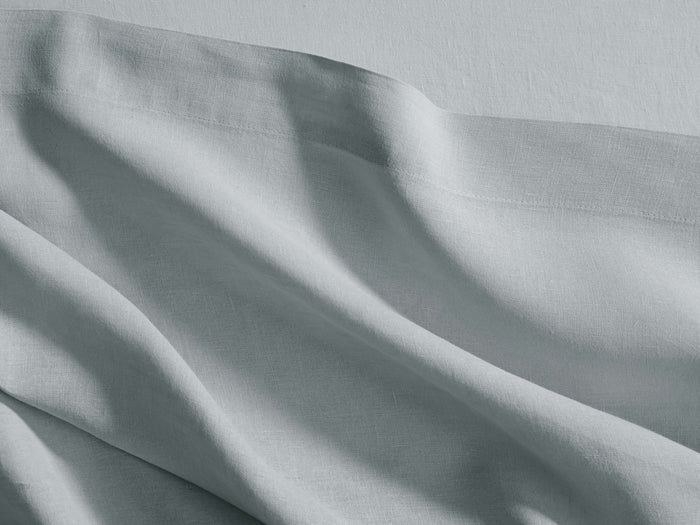 Soft light blue-grey Italian Garment-Dyed Linen Flat Sheet, draped with casual folds and a visible stitched hem.