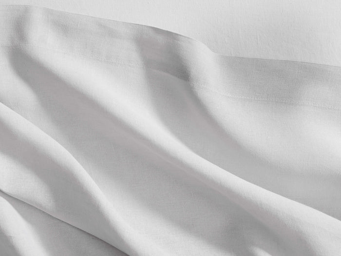 Close-up of white Italian Garment-Dyed Linen Flat Sheet, draped with soft folds, showing its natural texture & hem.