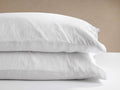 Two white Italian Garment-Dyed Linen Pillowcases, stacked on a white surface with a light beige wall behind them.