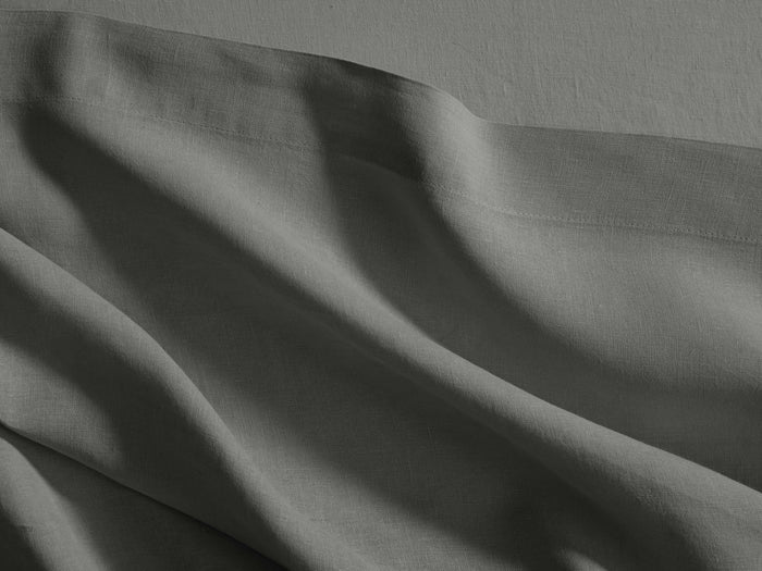 Charcoal Italian garment-dyed linen queen flat sheet, draped with soft wrinkles, highlighting its texture and a subtle hem.