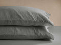 Two charcoal grey Italian garment-dyed linen standard pillowcases stacked, showing soft texture against a beige background.