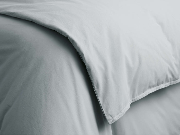 Close-up of a sky blue Italian garment-dyed percale duvet, showing a gentle fold, soft texture, and subtle creases.