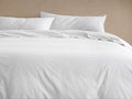 White Italian Garment-Dyed Percale Duvet Set, featuring a relaxed duvet cover and two pillow shams on a bed against a beige wall.