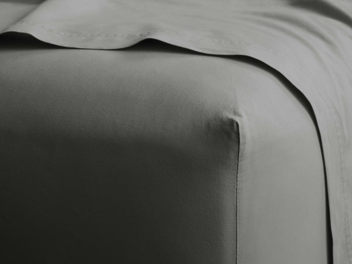Close-up of a gray Italian garment-dyed percale fitted sheet covering a bed corner, with a matching top sheet draped.
