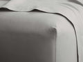 Close-up of a light gray Italian Garment-Dyed Percale Fitted Sheet, neatly covering a mattress, with a matching flat sheet draped above.