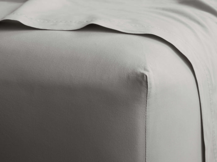 Close-up of a light gray Italian Garment-Dyed Percale Fitted Sheet, neatly covering a mattress, with a matching flat sheet draped above.
