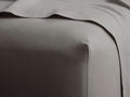 Angled close-up of a neutral gray Italian Garment-Dyed Percale Fitted Sheet on a mattress, with a matching top sheet folded.