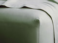 Light sage green Italian Garment-Dyed Percale Fitted Sheet on a bed, showing a crisp corner and coordinating top sheet folded.
