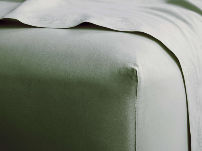 Light sage green Italian Garment-Dyed Percale Fitted Sheet on a bed, showing a crisp corner and coordinating top sheet folded.
