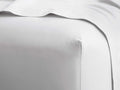 Close-up of a smooth, white Italian Garment-Dyed Percale Fitted Sheet on a mattress corner, with a matching top sheet draped.