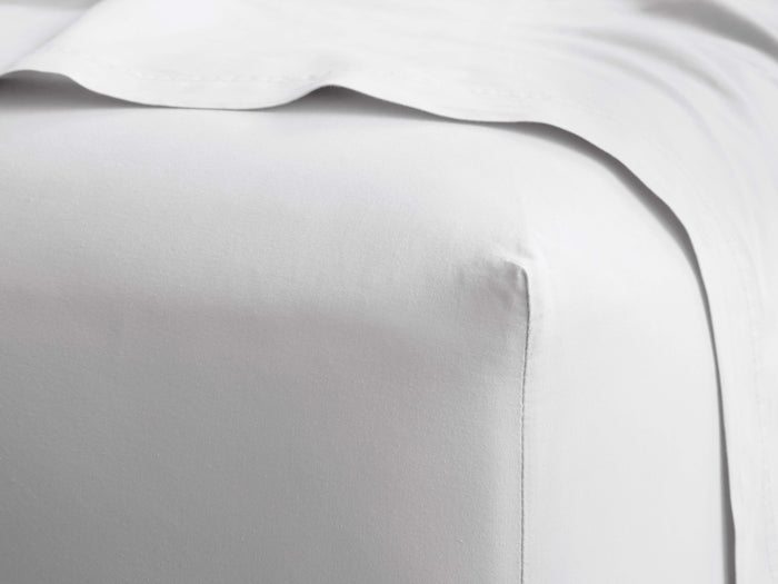 Close-up of a smooth, white Italian Garment-Dyed Percale Fitted Sheet on a mattress corner, with a matching top sheet draped.