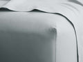Close-up of a sky blue Italian Garment-Dyed Percale King Fitted Sheet fitted neatly on a mattress, with a top sheet folded over.
