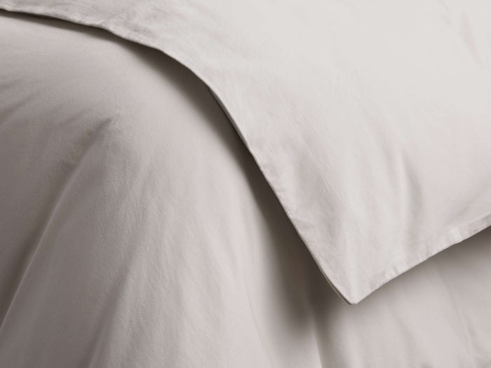 Natural Italian Garment-Dyed Sateen Duvet, close-up. Folded, smooth light gray fabric with subtle sheen and soft creases.