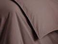 A close-up of a smooth, chocolate brown fabric with textured folds and stitched edges, likely part of a bedding set or garment.
