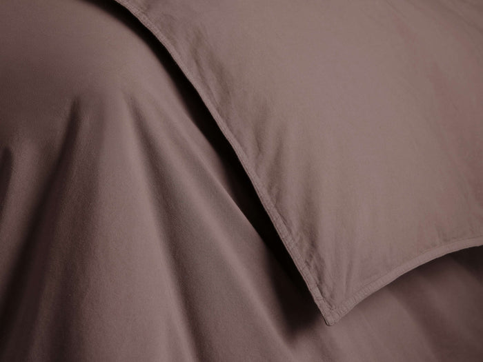 A close-up of a smooth, chocolate brown fabric with textured folds and stitched edges, likely part of a bedding set or garment.